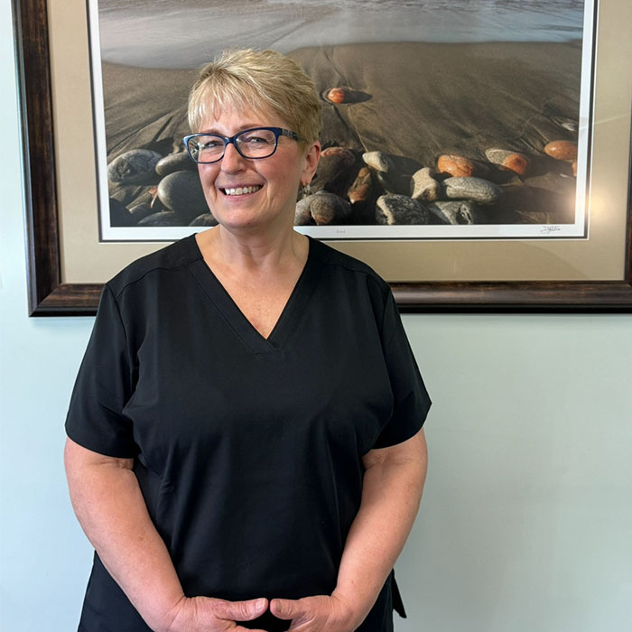 A woman in a black shirt and glasses, standing in front of a framed picture with a beach scene.