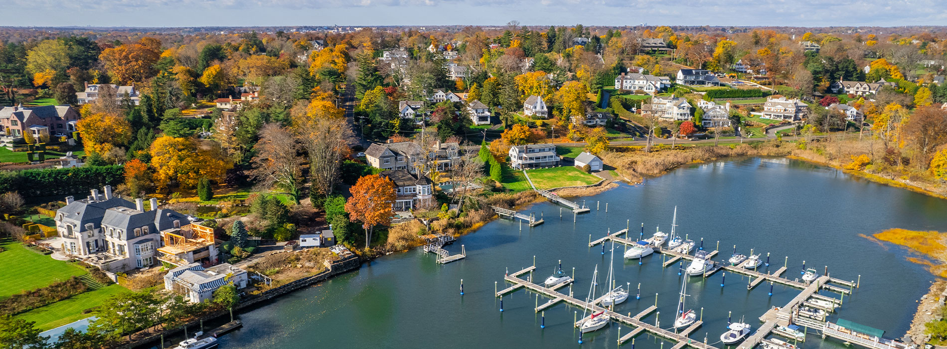 Aerial view of a serene residential area with houses, docks, boats, and autumnal trees surrounding a lake.