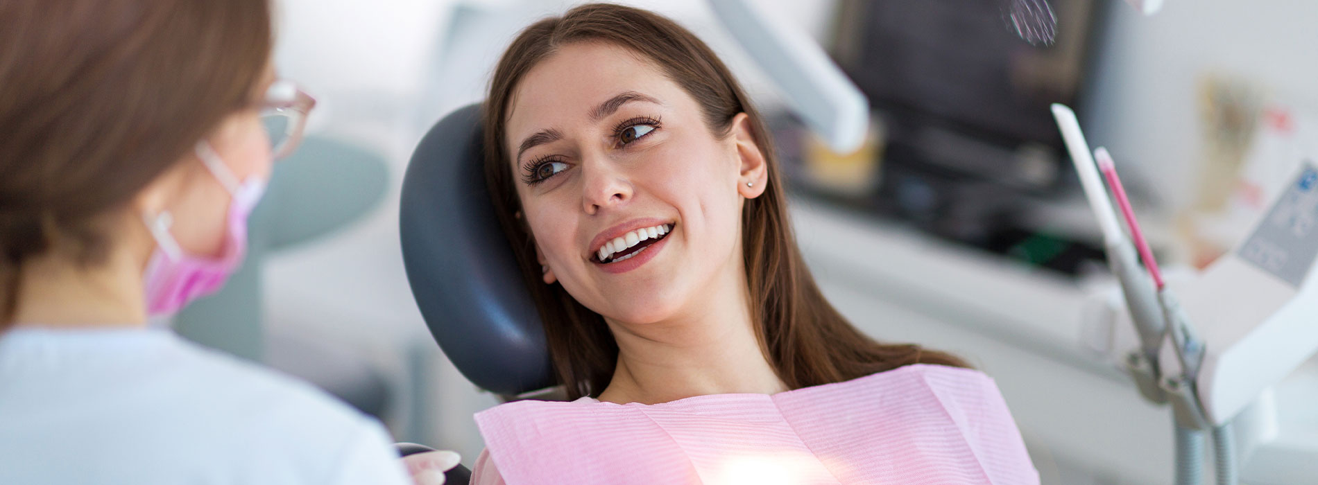 Woman in dental chair receiving treatment, smiling at camera with professional behind her.