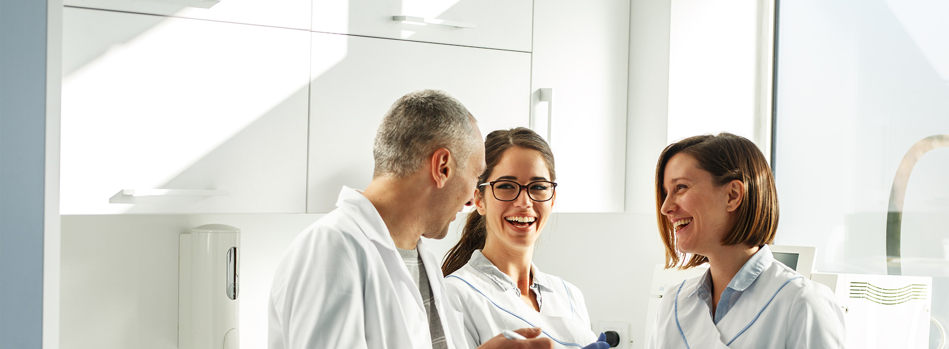 The image depicts a group of individuals, likely professionals in a medical or dental setting, gathered around a counter with a smiling man and woman, possibly discussing something.