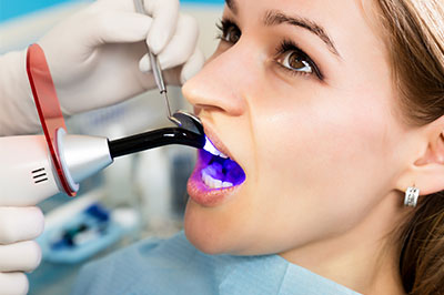 A dental professional using a device to examine a patient s teeth while the patient is seated in a chair.