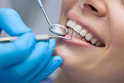 The image shows a person in the process of receiving dental care, with a focus on a smiling mouth being worked on by a dental professional using dental instruments.