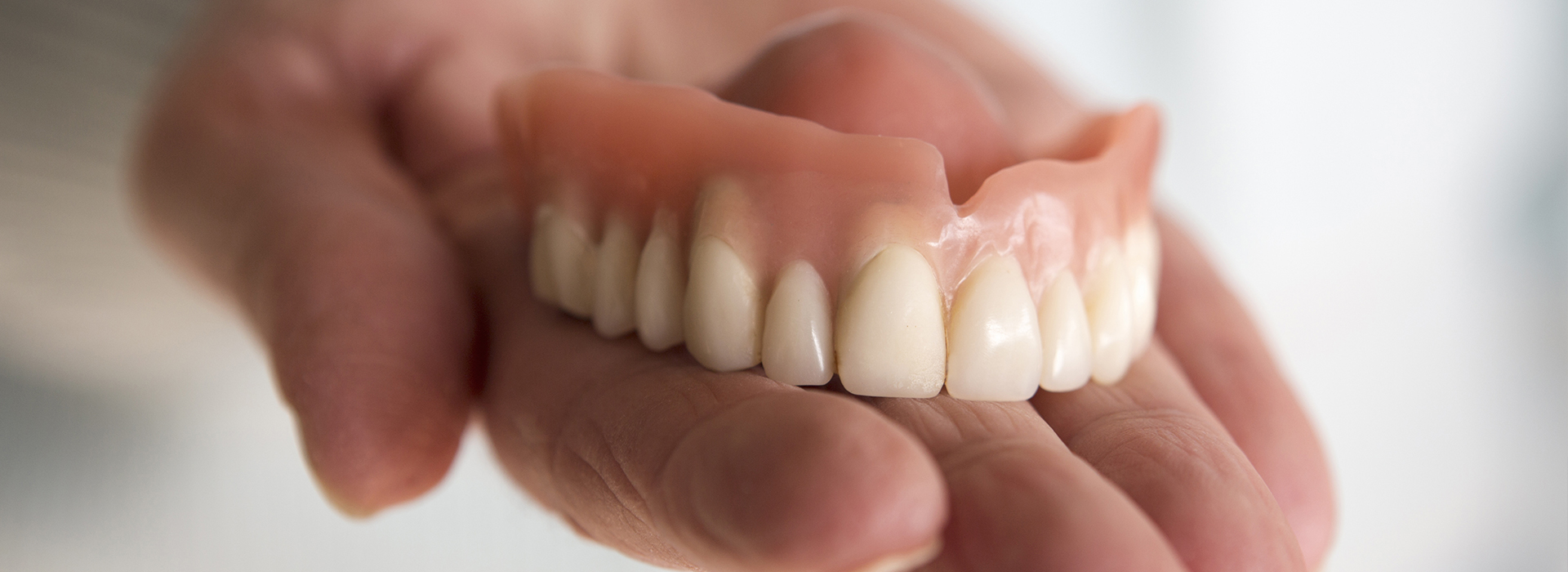 The image features a hand holding up a set of dentures, showcasing the upper and lower teeth.