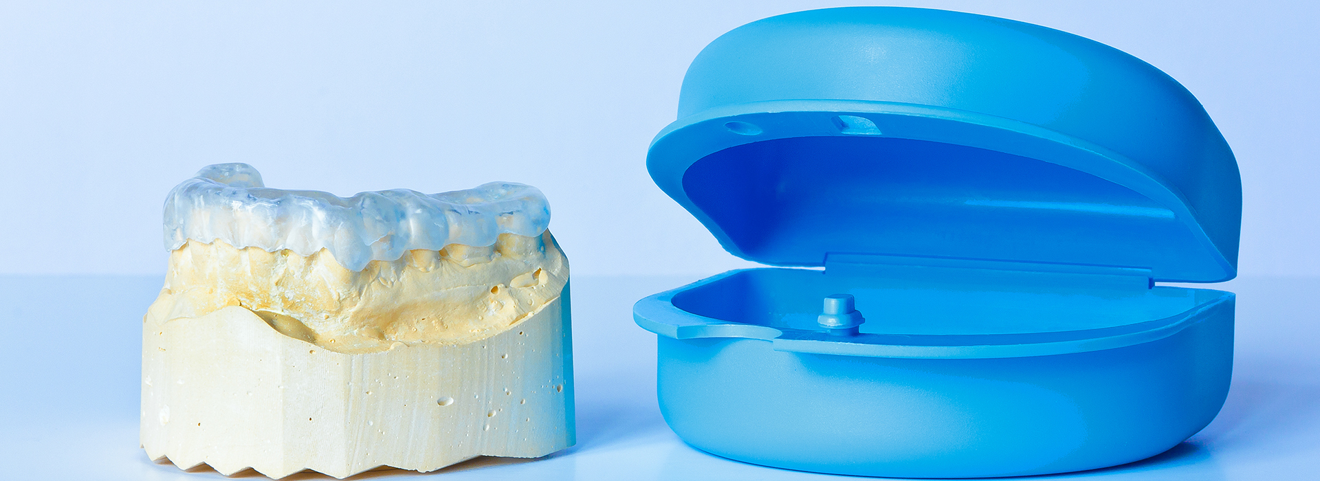 The image shows a blue toothbrush on the left and a yellow dental mold on the right, both placed against a white background.