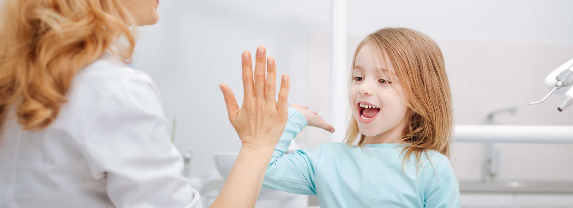 A woman in a white lab coat is interacting with a child, likely in a dental or medical setting.