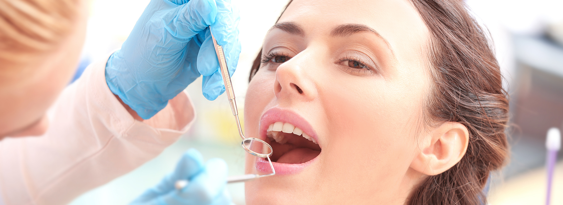 The image shows a person receiving dental treatment, with a dentist in the process of placing a crown using a drill and other dental instruments.