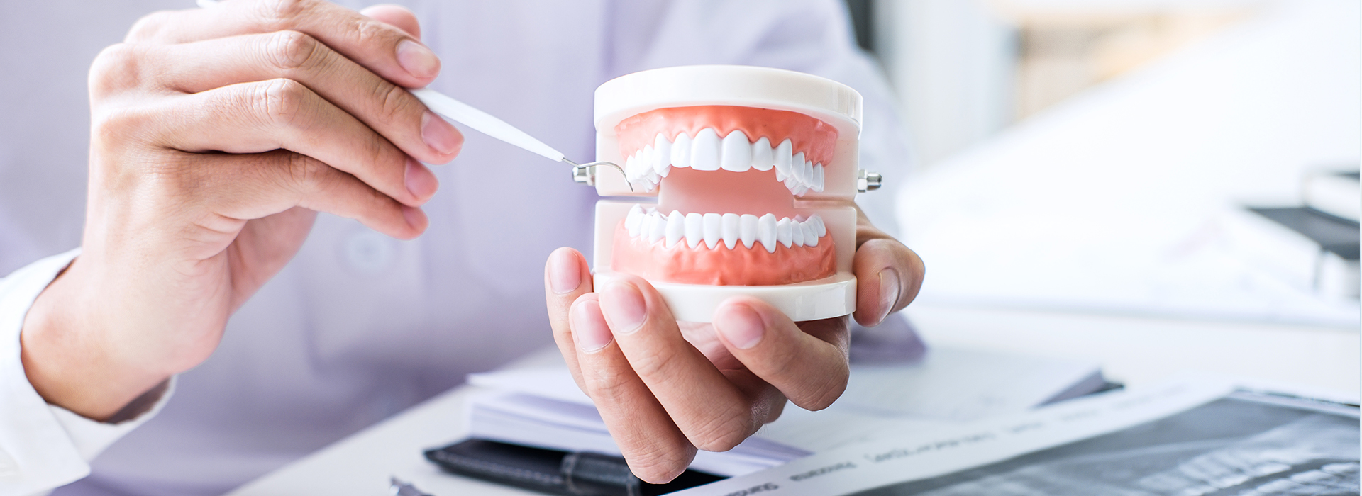 An individual holding a toothbrush and toothpaste in front of a blurred background, likely to be a dental office.