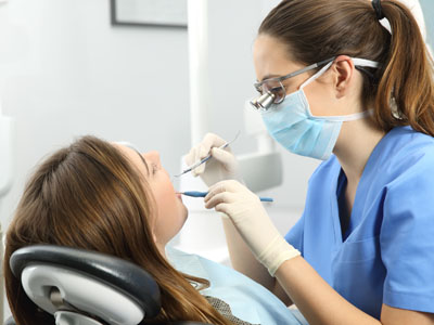 A dental professional is performing a procedure on a patient in an office setting, with the patient seated and receiving treatment.