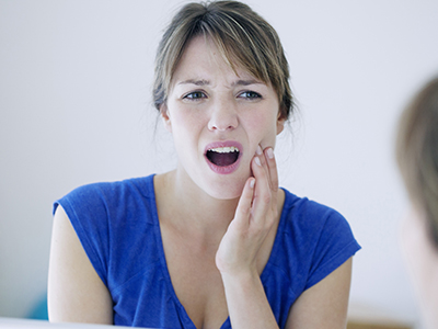 A woman with a surprised expression is looking at her reflection in the mirror, holding her hand to her mouth.