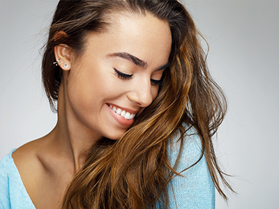 A smiling woman with long hair, wearing a blue top and earrings.