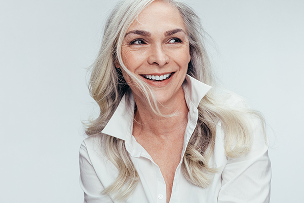 Woman with blonde hair and a white shirt smiling against a neutral background.