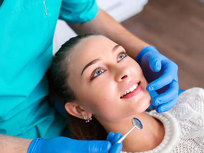 A dental hygienist is performing a teeth cleaning procedure, with a smiling patient wearing a blue surgical mask.