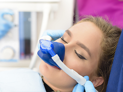 A woman receiving oxygen therapy with a medical device attached to her face, attended by a healthcare professional in a clinical setting.