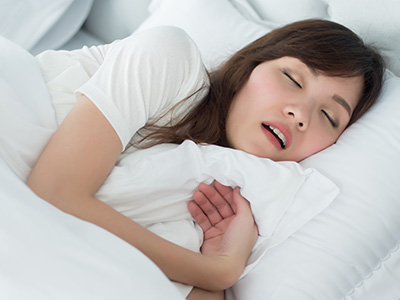 A woman is lying in bed, holding her chest with one hand and appears to be asleep.