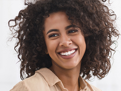 The image is of a woman with curly hair, smiling and looking directly at the camera.